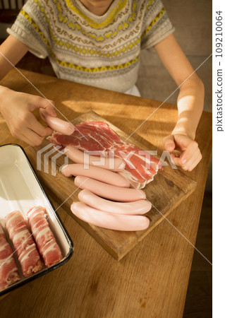 A girl prepares a traditional Christmas dish "Pigs in a blanket" Wraps sausages in bacon 109210064
