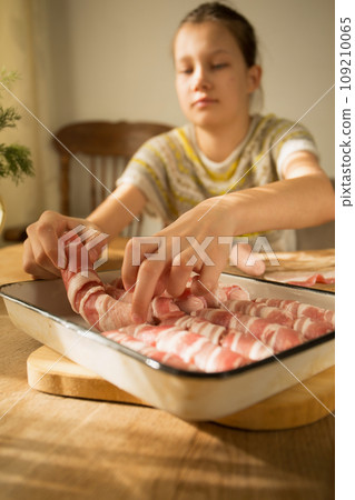 A girl prepares a traditional Christmas dish "Pigs in a blanket" Wraps sausages in bacon 109210065