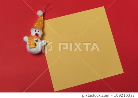snowman and blank yellow sheet of paper on a red background, christmas concept snowman and blank yellow sheet of paper on a red background, christmas concept 109210352