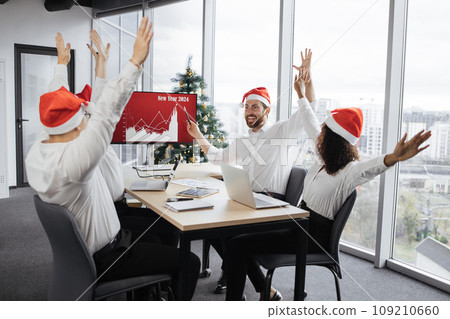 Successful team of multiethnic business people in Santa hats raising hands Successful team of multiethnic business people in Santa hats raising hands 109210660