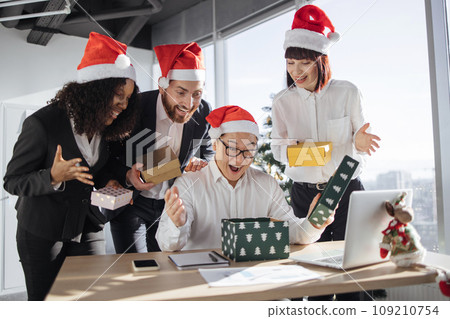 Asian businessman in Santa hat unpacks a Christmas present from multinationals colleagues 109210754