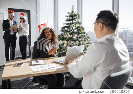 Happy african businesswoman in Santa hat working on laptop with asian client. 109210805
