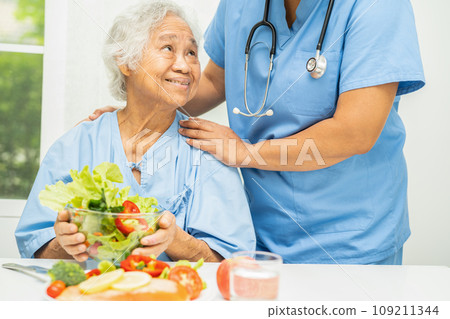 Asian elderly woman patient eating salmon steak breakfast with vegetable healthy food in hospital. 109211344
