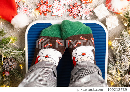 A woman in Christmas socks stands on the scales, weighs herself after gluttony during the holidays A woman in Christmas socks stands on the scales, weighs herself after gluttony during the holidays 109212789