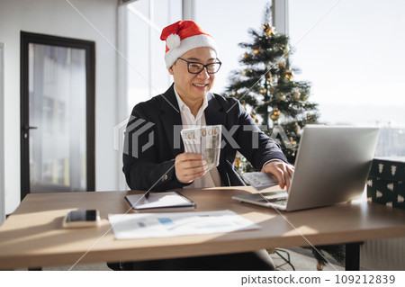 asian male accountant in Santa hat holding cash banknotes. 109212839