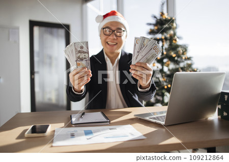 Asian man in Santa hat showing hands with cash papers counting money 109212864