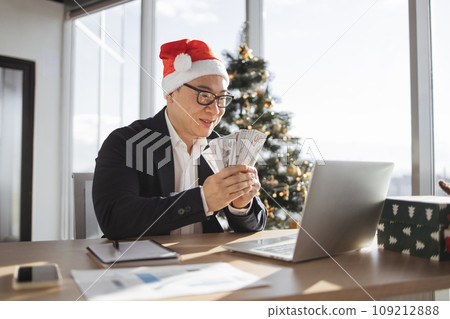 Adult asian rich business man in Santa hat working on laptop counting money cash 109212888
