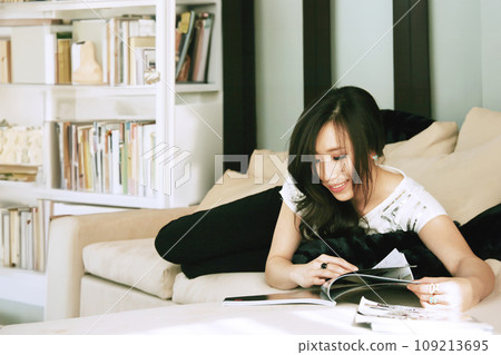 Happy single Asian womanlook at magazines alone in the house Happy single Asian womanlook at magazines alone in the house 109213695