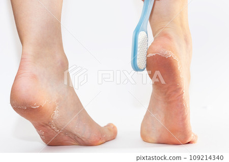 Close-up of women's feet, with pumice stone with peeling leather soles on heels. White background. Skin care and pedicure 109214340