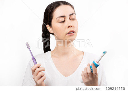 Portrait of young Caucasian woman with ligature braces on her teeth, choosing between an electric and manual toothbrush. Concept of orthodontic treatment and dental care 109214350