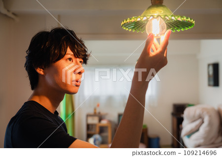 Young man replacing an incandescent light bulb 109214696