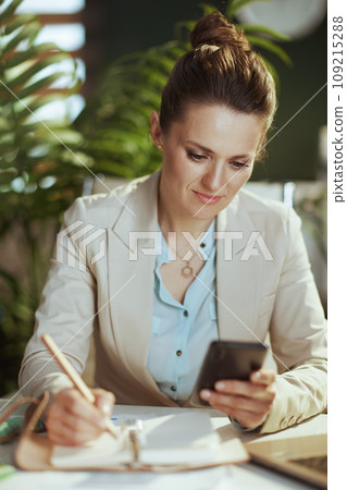 modern female employee in modern green office using smartphone modern female employee in modern green office using smartphone 109215288