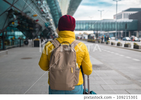 Happy attractive 60s senior female traveler walking with a suitcase at the modern transport stop outdoors near the modern airport terminal Happy attractive 60s senior female traveler walking with a suitcase at the modern transport stop outdoors near the modern airport terminal 109215301
