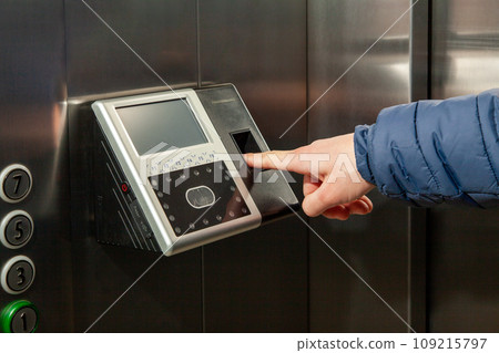 The man put his finger in the Fingerprint Access Control Terminal with face recognition function installed in the elevator of the business center 109215797