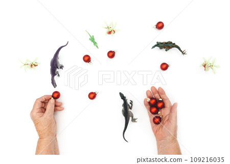 Happy new year 2024 year of dragon. Dinosaurs and Old hands holding red Christmas toys on white background. Christmas concept. Copy Space for text. Front view. Happy new year 2024 year of dragon. Dinosaurs and Old hands holding red Christmas toys on white background. Christmas concept. Copy Space for text. Front view. 109216035