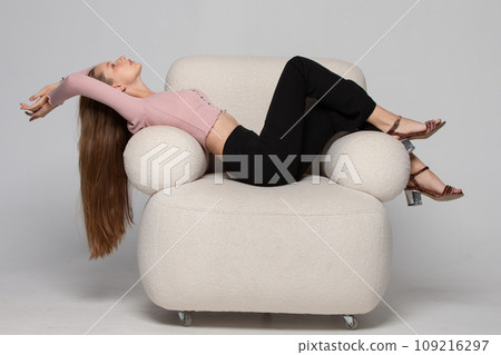 A beautiful slender girl with long blond hair lies in a comfortable white chair. A woman rests and relaxes in a chair. A beautiful slender girl with long blond hair lies in a comfortable white chair. A woman rests and relaxes in a chair. 109216297