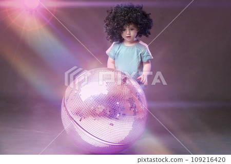 A little funny girl looks with admiration at a shiny pink disco ball. 109216420