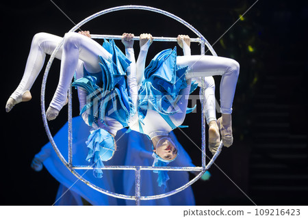 Two acrobat girls show a circus number on a dark background. Acrobatic performance. 109216423