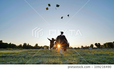 Cheerful graduates students run throwing notebooks after school at sunset. Cheerful graduates students run throwing notebooks after school at sunset. 109216490
