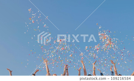 Tossing colorful paper confetti from the hands of young people. 109216584