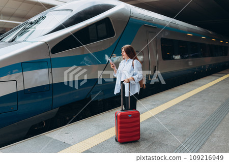 Young redhead woman waiting train with backpack and using smart phone. Railroad transport concept, Traveler. 30s Woman with suitcase walking at railroad station platform. Travel to vacation by train Young redhead woman waiting train with backpack and using smart phone. Railroad transport concept, Traveler. 30s Woman with suitcase walking at railroad station platform. Travel to vacation by train 109216949
