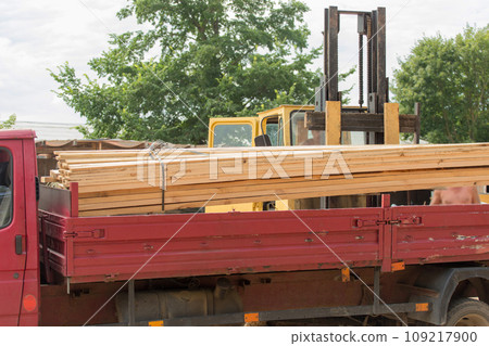 A forklift loads wooden planks into the back of a trailer car. Wood industry A forklift loads wooden planks into the back of a trailer car. Wood industry 109217900
