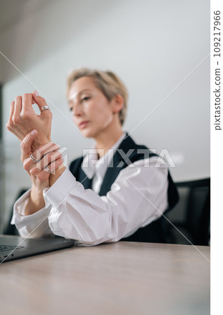 Vertical shot of exhausted middle-aged business woman feeling severe wrist arm pain while overwork typing on laptop computer at workplace. Mature female manager tired massaging hand. Vertical shot of exhausted middle-aged business woman feeling severe wrist arm pain while overwork typing on laptop computer at workplace. Mature female manager tired massaging hand. 109217966