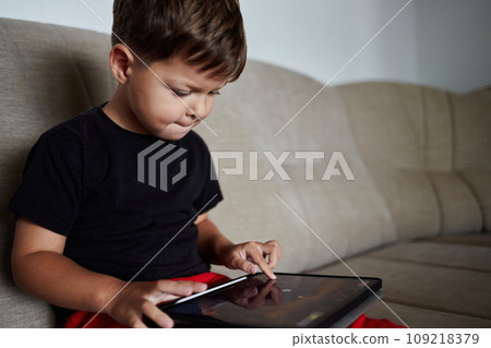 Toddler plays video games on a tablet at home. Toddler plays video games on a tablet at home. 109218379