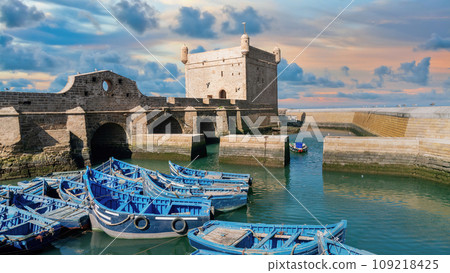 Sqala du Port with dramatic clouds, a historic fortress overlooking the Atlantic Ocean at the fishing port of Essaouira with many seagulls flying overhead, Morocco. 109218425