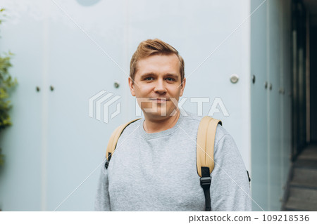 A handsome young man with backpack walking on the street in the city. Urban lifestyle concept. Traveler. Portrait of happy 30s man in casual clothing looking at camera outdoor. A handsome young man with backpack walking on the street in the city. Urban lifestyle concept. Traveler. Portrait of happy 30s man in casual clothing looking at camera outdoor. 109218536