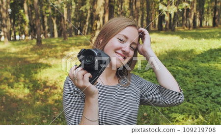A young girl photographer with a camera poses in the park. A young girl photographer with a camera poses in the park. 109219708