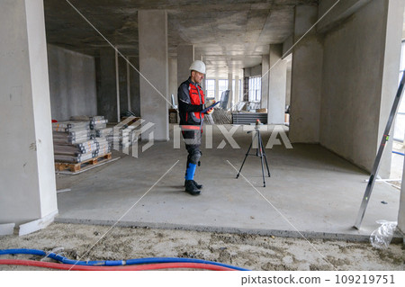 A foreman at a construction site in work clothes controls the work process, takes the necessary measurements A foreman at a construction site in work clothes controls the work process, takes the necessary measurements 109219751