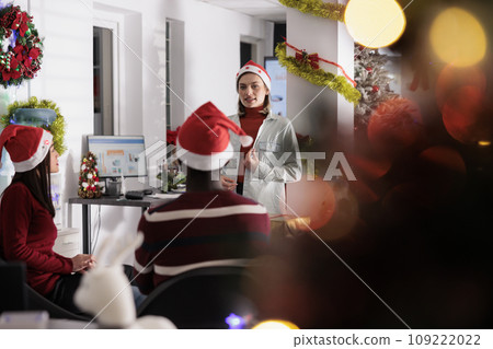 Manager having relaxed chat with employees, discussing year end business matters before Christmas holiday season. MAnagement executive talking with company personnel in festive adorn office 109222022