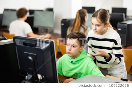 Teen schoolgirl talking to focused classmate in computer class 109222036
