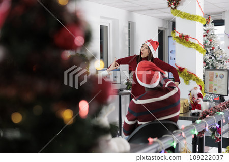 Asian employee having fun at work with coworkers, playing charades in festive decorated office during Christmas holiday season. Staff members laughing together in xmas ornate workspace Asian employee having fun at work with coworkers, playing charades in festive decorated office during Christmas holiday season. Staff members laughing together in xmas ornate workspace 109222037