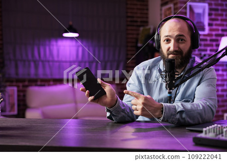 Portrait of tech vlogger reviewing newly released smartphone in rgb lights living room studio. Entertaining content creator filming technology channel episode using professional video tools 109222041