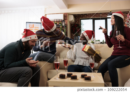 Cheerful excited african american woman employee holding xmas gift and guessing secret santa in office. Diverse colleagues drinking alcohol and sharing christmas presents Cheerful excited african american woman employee holding xmas gift and guessing secret santa in office. Diverse colleagues drinking alcohol and sharing christmas presents 109222054