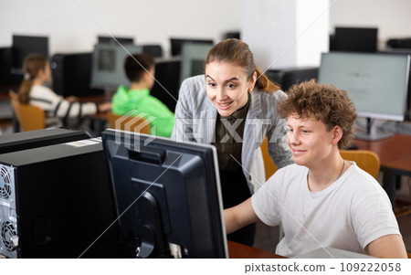 Smiling female teacher talking to cheerful teenager studying in computer lab 109222058