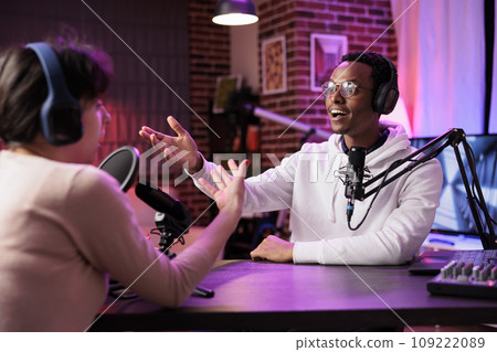 African american podcast host discussing with guest during live broadcast for social media website, being surprised by her knowledge. Internet star chatting with woman during online stream African american podcast host discussing with guest during live broadcast for social media website, being surprised by her knowledge. Internet star chatting with woman during online stream 109222089