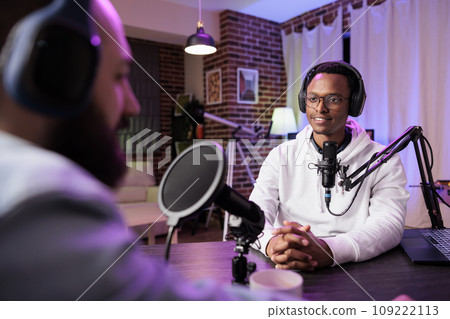 Podcast presenter having live conversation with man, recording discussion for audience on internet entertainment show. Influencer enjoying chat with guest, broadcasting at home 109222113