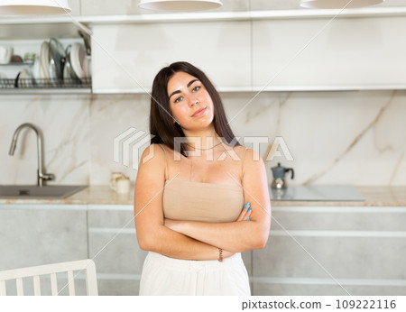 Smiling young woman posing against background of white kitchen Smiling young woman posing against background of white kitchen 109222116