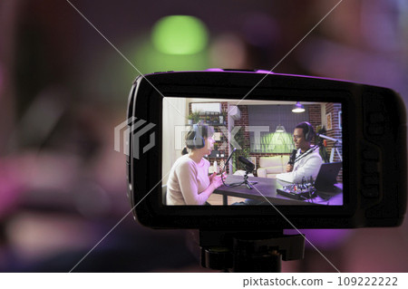 Close up shot focused on preview image on professional camera with podcast host and african american guest enjoying conversation in blurry background. Professional recording equipment in home studio Close up shot focused on preview image on professional camera with podcast host and african american guest enjoying conversation in blurry background. Professional recording equipment in home studio 109222222