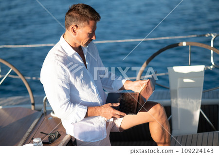 Successful mature man with a laptop working on a yacht Successful mature man with a laptop working on a yacht 109224143