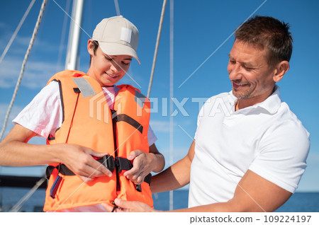 Father putting a life-jacket on his boy while sailing on the yacht Father putting a life-jacket on his boy while sailing on the yacht 109224197