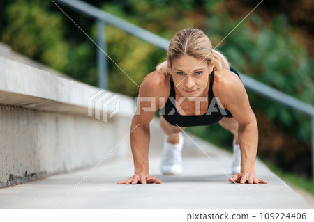 Blonde woman doing push ups outdoor. 109224406