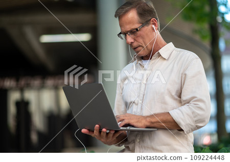 Middle aged man using laptop computer on city street. 109224448