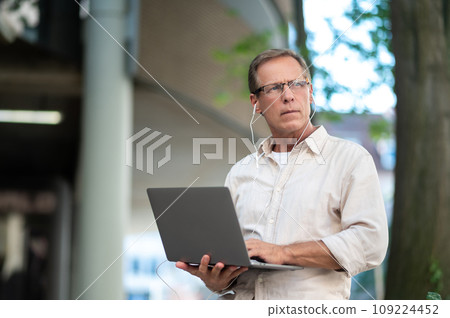 Middle aged man using laptop computer on city street. 109224452