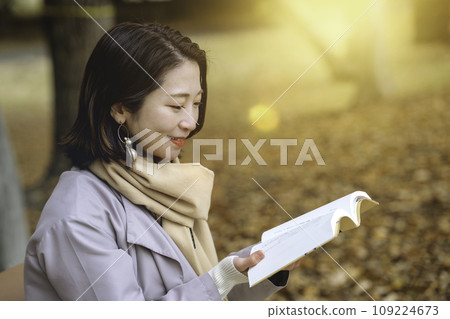 A woman reading on a bench in a park with autumn leaves A woman reading on a bench in a park with autumn leaves 109224673