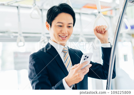 A middle-aged businessman looking at his smartphone on a commuter train. Photo provided by Keio Electric Railway Co., Ltd. 109225809