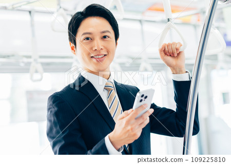 A middle-aged businessman looking at his smartphone on a commuter train. Photo provided by Keio Electric Railway Co., Ltd. 109225810